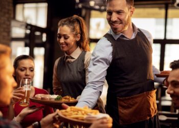 Young waiters serving lunch to group of friends in a pub.